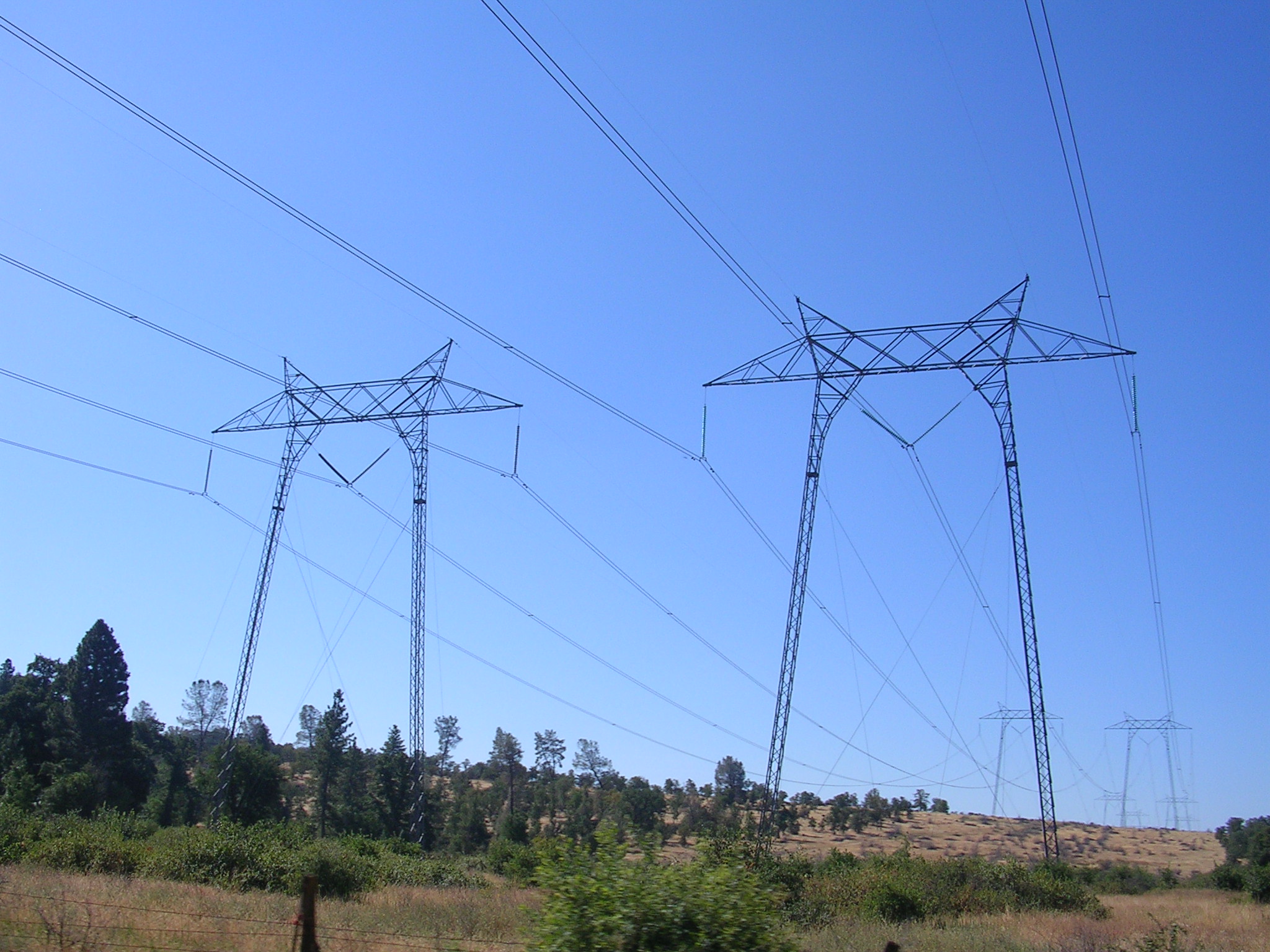 PG&E 500 kV transmission towers crossing State Route 36 through dry foothill woodland under a clear blue sky, Tehama County, California